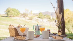 En picnicopstilling med en kurv, kaffekande og drikkevarer på et bord udendørs.
