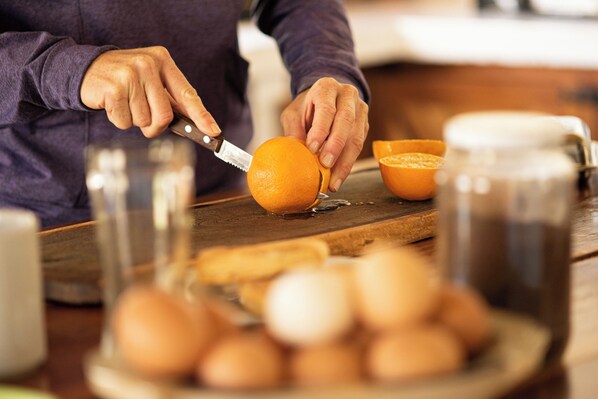 A person cutting an orange on a wooden cutting board with a knife. - Loma Puskana-Casas (Cachi)