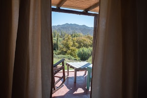 Vista a través de un vano de puerta que da a un patio con mesa y sillas, con vistas a un paisaje montañoso.