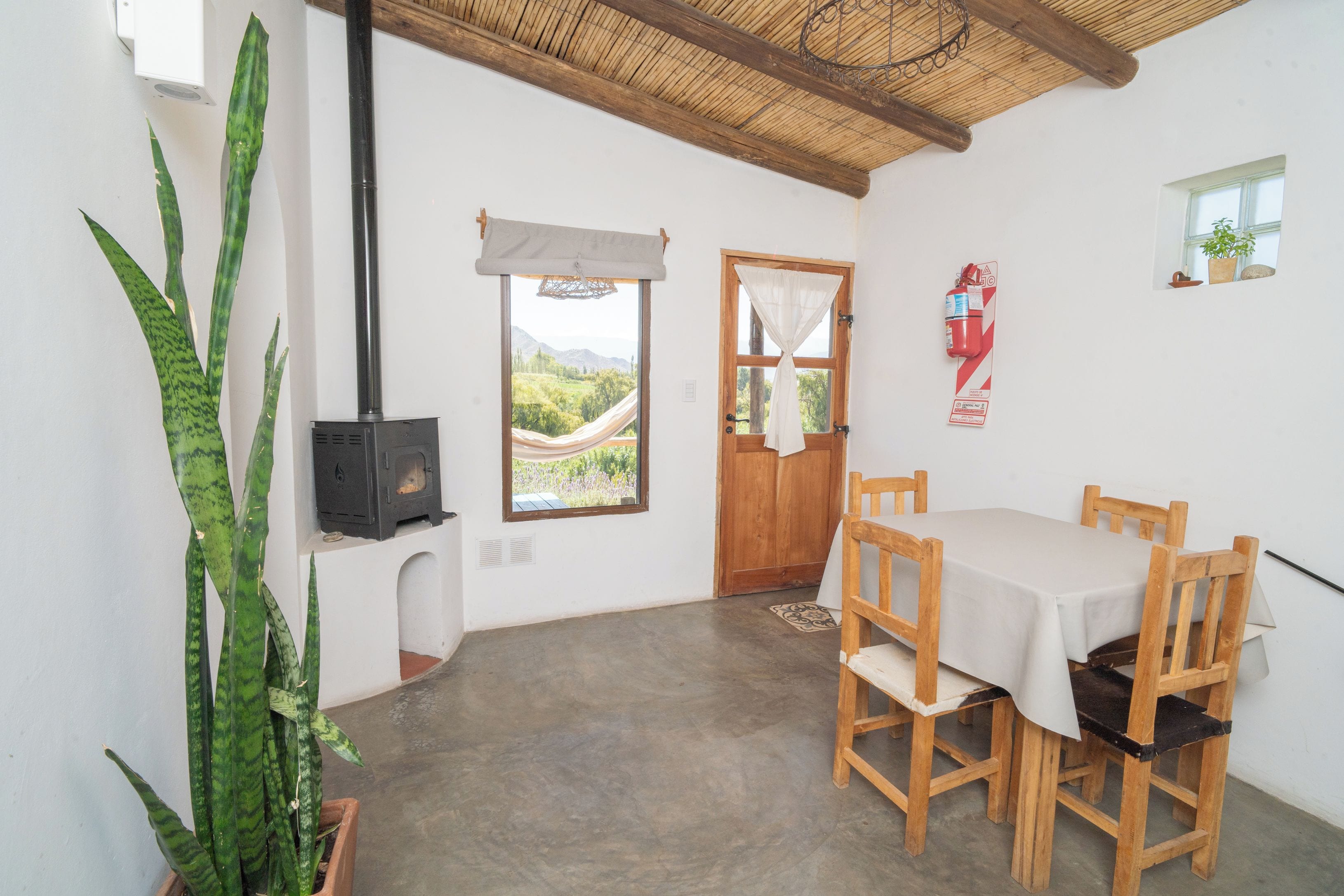 A room with a table, chairs, a fireplace, a window with a view, and a potted plant.