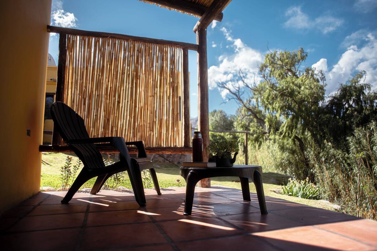 Eine Terrasse mit zwei Stühlen und einem Tisch, einem Bambuszaun und Blick auf Grünflächen sowie ein Gebäude im Hintergrund.