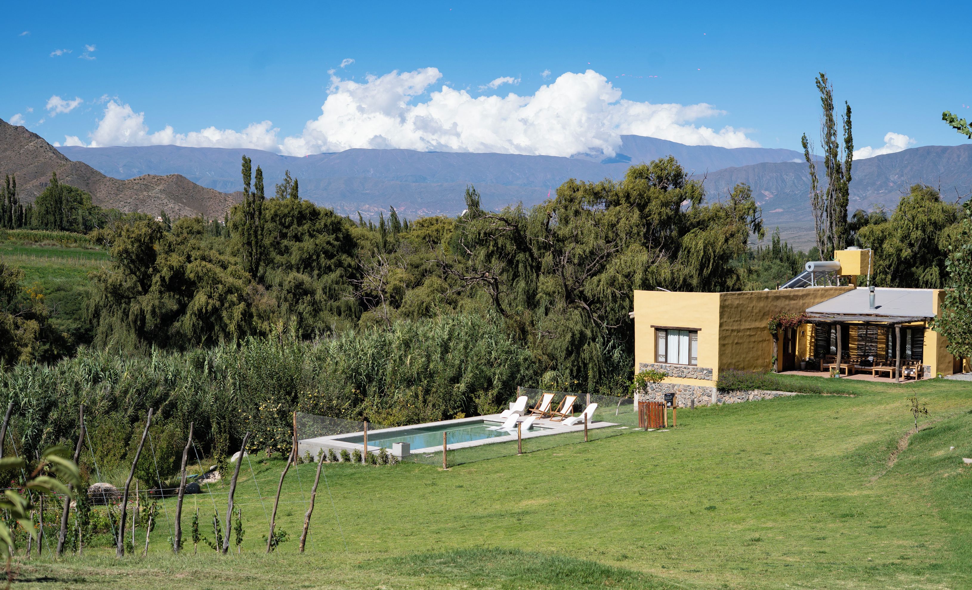A pool area with lounge chairs, a small building with a sloped roof, and a mountainous backdrop.
