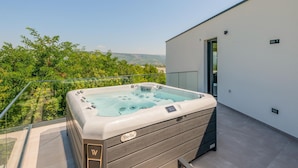 Banheira de hidromassagem em varanda, com vista desobstruída para vegetação e colinas ao longe.