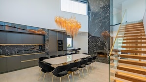 Uma área de jantar moderna com painel de fundo de mármore, um lustre grande e uma escada com degraus de madeira.