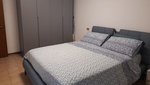 Una camera da letto con un letto, un armadio grigio e una parete semplice.