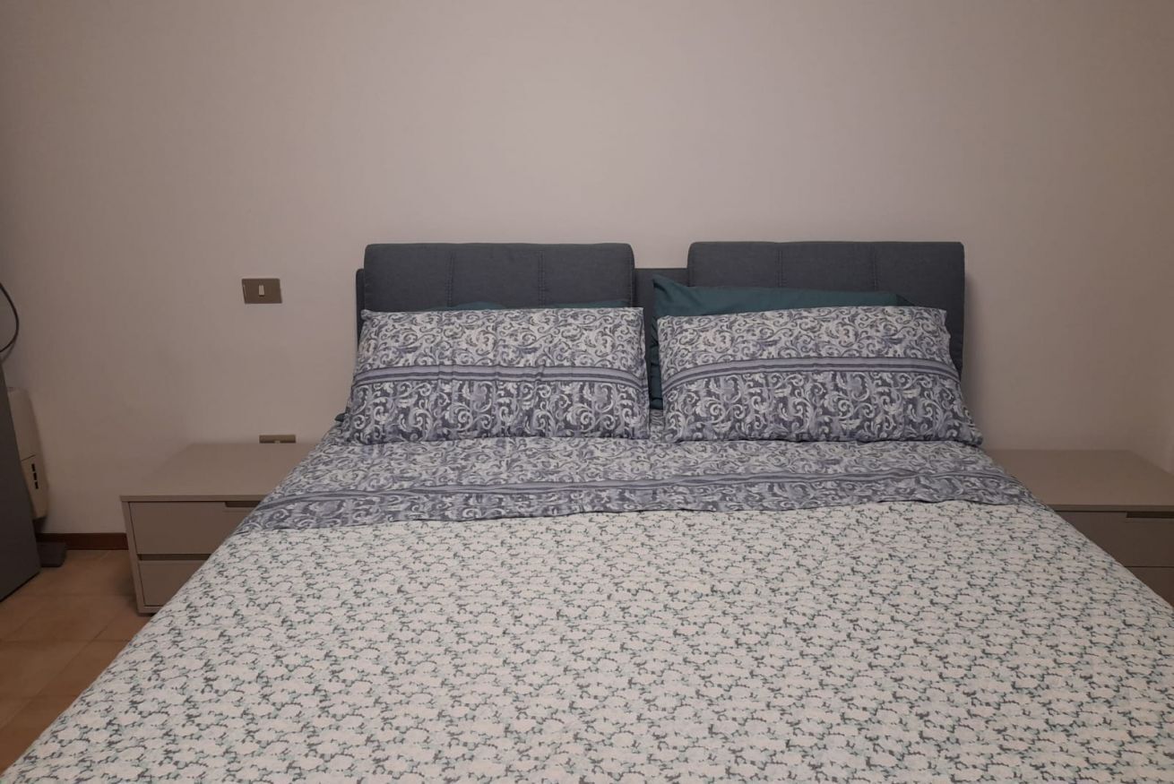 A bed with patterned bedding, a bedside table, and a wall socket.