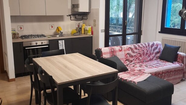 Una cucina compatta con tavolo e sedie, un divano e vista panoramica attraverso una porta vetrata.