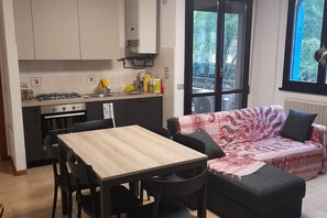 Eine kompakte Küche mit Esstisch und Stühlen, einer Couch und Blick durch eine Glastür.