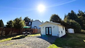 A small white building with a black door, a gravel driveway, and a wooden fence in a backyard. - Modern studio in MarysVille – A Forest Haven (Marysville)