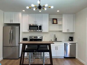 A modern kitchen with white cabinets, stainless steel appliances, a wooden table, and bar stools. - Modern studio in MarysVille – A Forest Haven (Marysville)