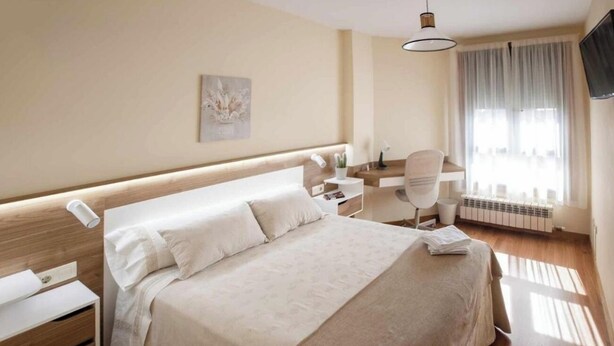 A hotel room with a large bed, a desk with a chair, a flat-screen TV, and a window with curtains. - Apartment 5 minutes from the historic center of Pontevedra (Pontevedra)