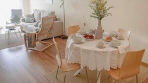 A dining area with a round table set for four, surrounded by chairs. A vase with flowers is on the table, and there is a sofa and a floor lamp in the background. - Apartment 5 minutes from the historic center of Pontevedra (Pontevedra)