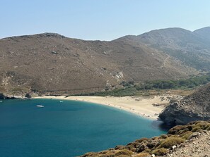 Ett kustlandskap med en strand, klart blått vatten och bergiga kullar.