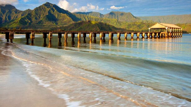 Un muelle se adentra en aguas tranquilas con montañas al fondo.