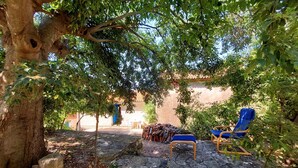 A stone patio with two blue chairs, a pile of firewood, and a rustic building in the background. - Nice home in Koromacno (Koromacno)