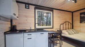 Habitació senzilla amb petita cuina, un llit i finestra amb vista al bosc.