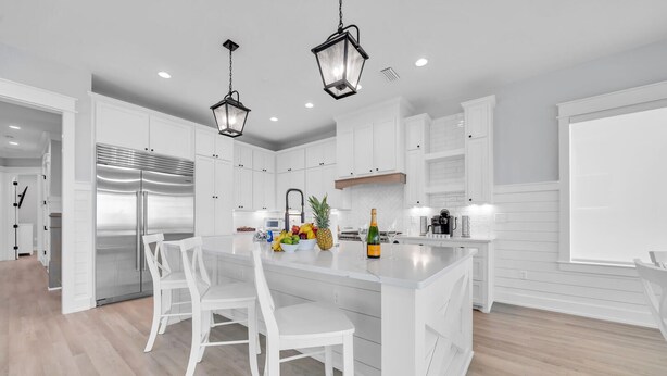 Una cocina moderna con armarios blancos, un refrigerador de acero inoxidable y una isla central con asientos.