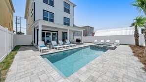 Una piscina rectangular con borde de azulejos, rodeada de sillones de descanso y un área de patio techada.