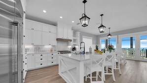 Una cocina moderna con armarios blancos, una isla grande e iluminación colgante.