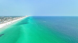 Vista aérea de una zona costera con playa, edificios y un mar azul cristalino.