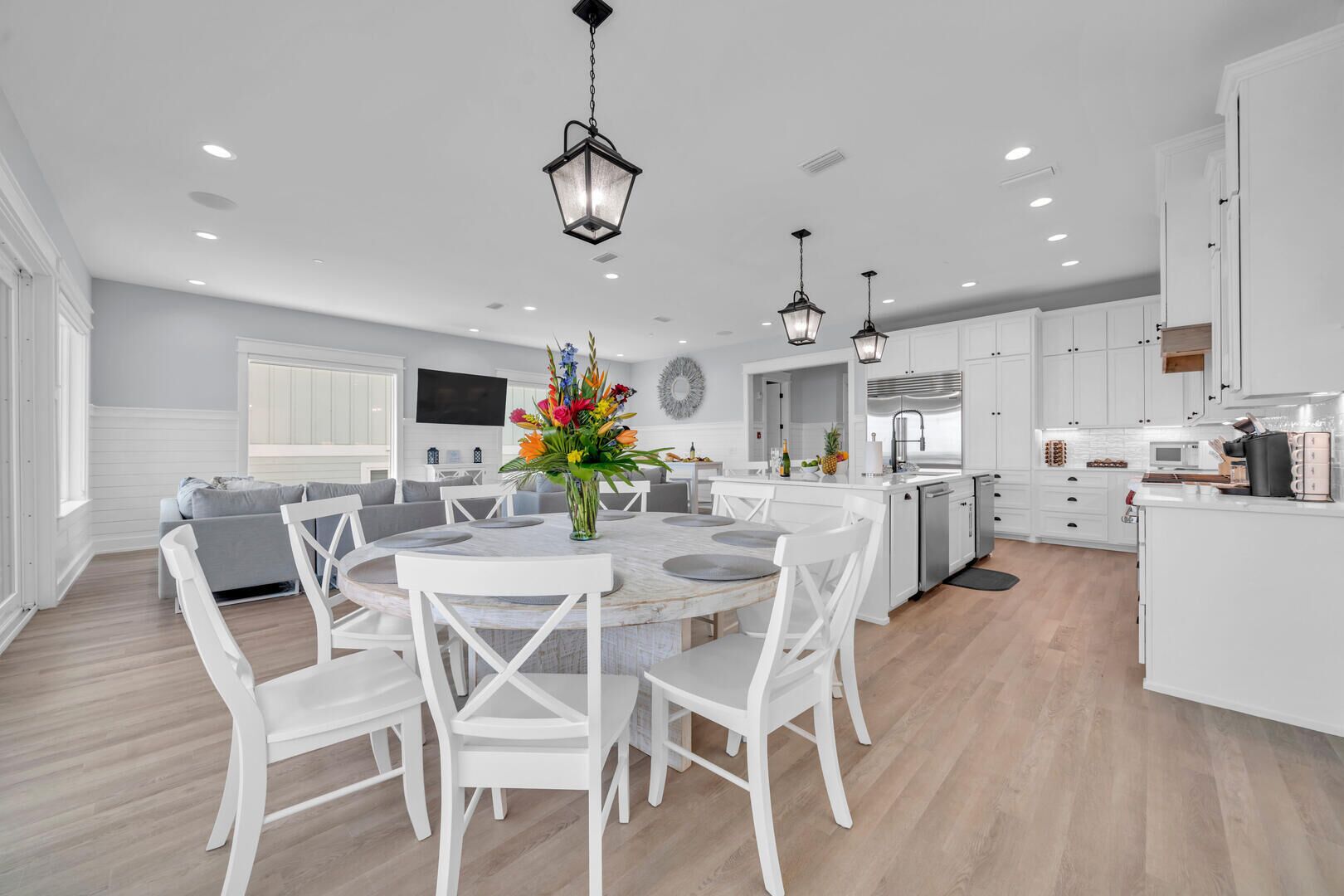 A modern kitchen with white cabinetry, a central island, and a dining area with white chairs and a round table.