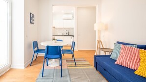 Een moderne woonkamer met een blauwe bank, kleurrijke kussens en een gestreept vloerkleed.