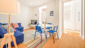 Een moderne woonkamer met een blauwe bank, een ronde eettafel met blauwe stoelen en een lamp.