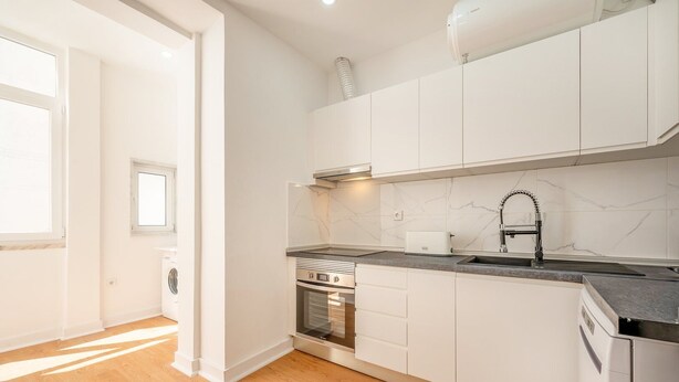 Een moderne keuken met witte kastjes, een inbouwoven, een roestvrijstalen spoelbak en een raam dat voor natuurlijk licht zorgt.