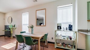 Un coin repas avec une table en bois et des chaises vertes, une petite plante en pot et un espace dédié au café, comprenant une bouilloire et des tasses.
