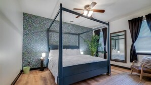 Un lit à baldaquin avec un ventilateur de plafond, une plante verte et un miroir au mur.