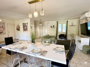 A dining area with a white table set for four, clear chairs, and hanging pendant lights.