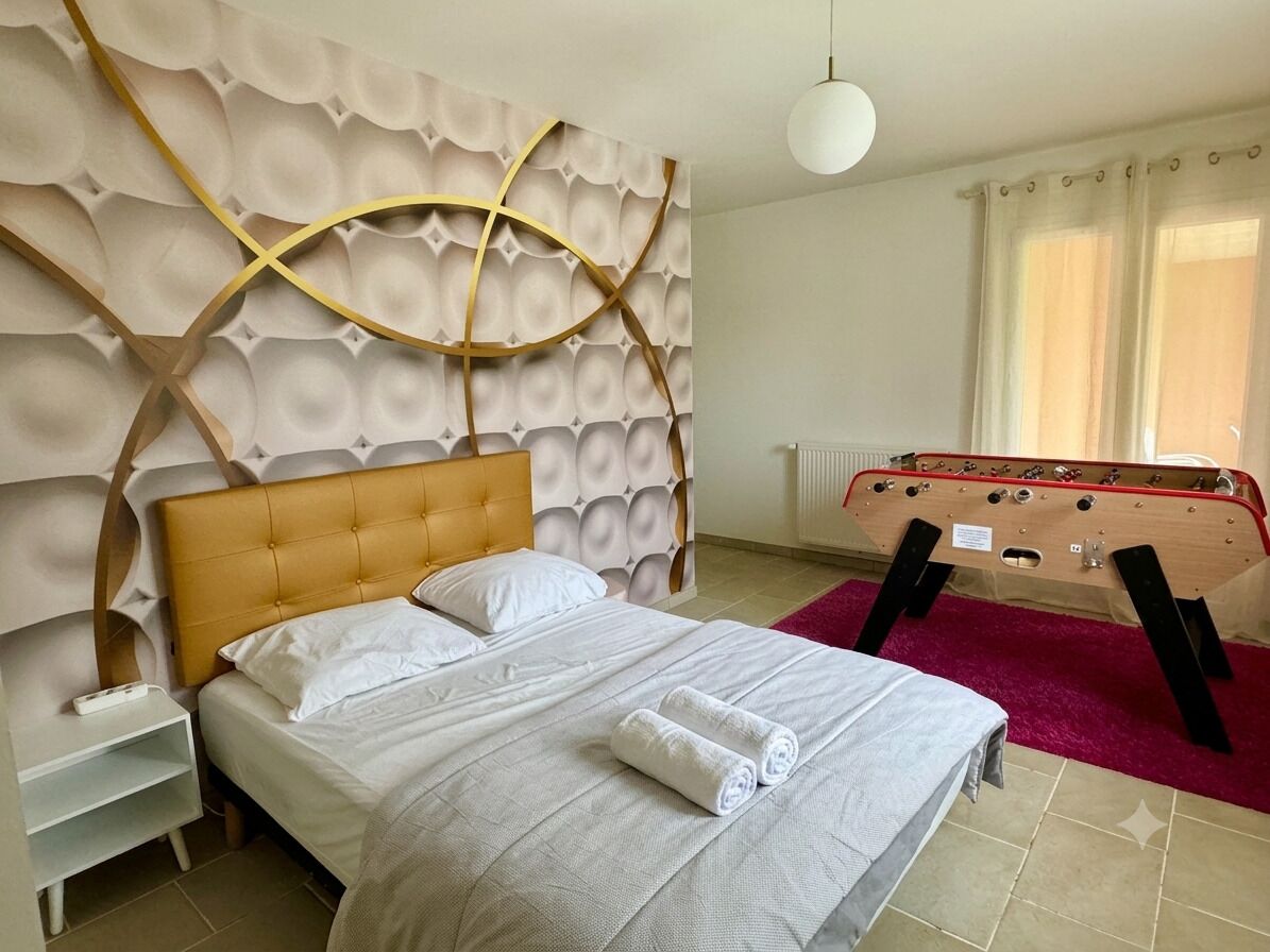 A hotel room with a bed, a headboard with a geometric pattern, a pool table, and a window with curtains.