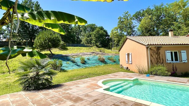 Ett hus med en swimmingpool, omgivet av en trädgård och träd.