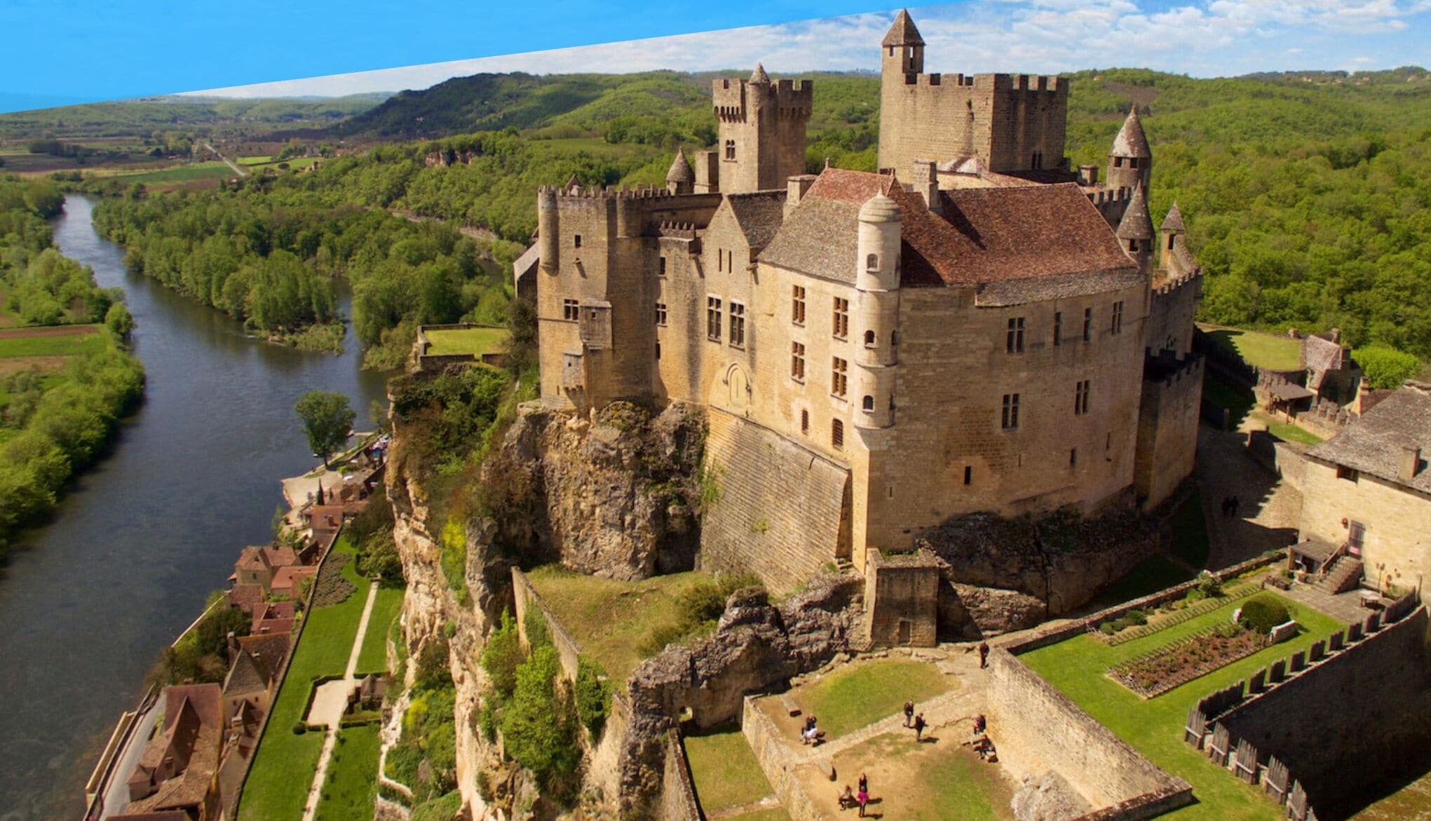 Un château historique, avec une rivière en arrière-plan, entouré d’une végétation luxuriante.