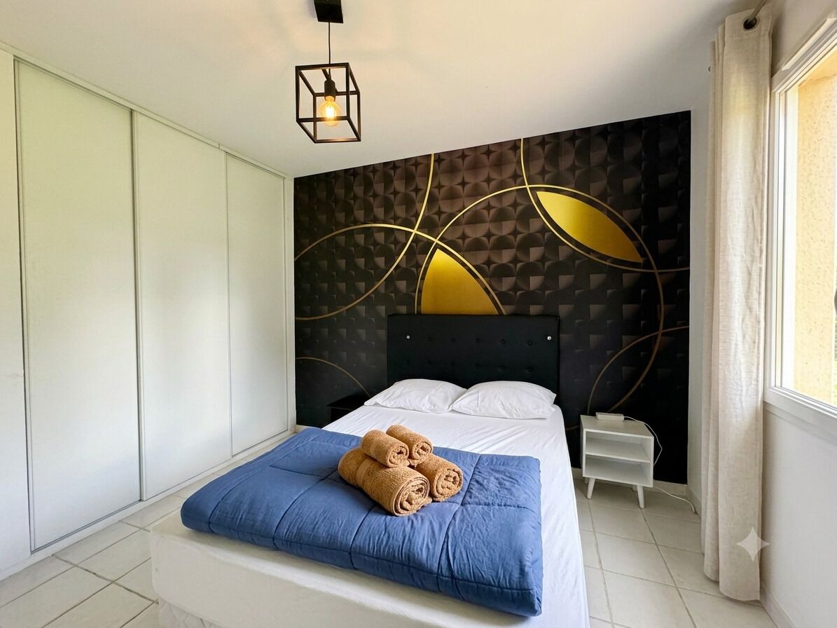 Ein Schlafzimmer mit Bett, Nachttisch, Kleiderschrank und einer Wand mit geometrischem Muster.