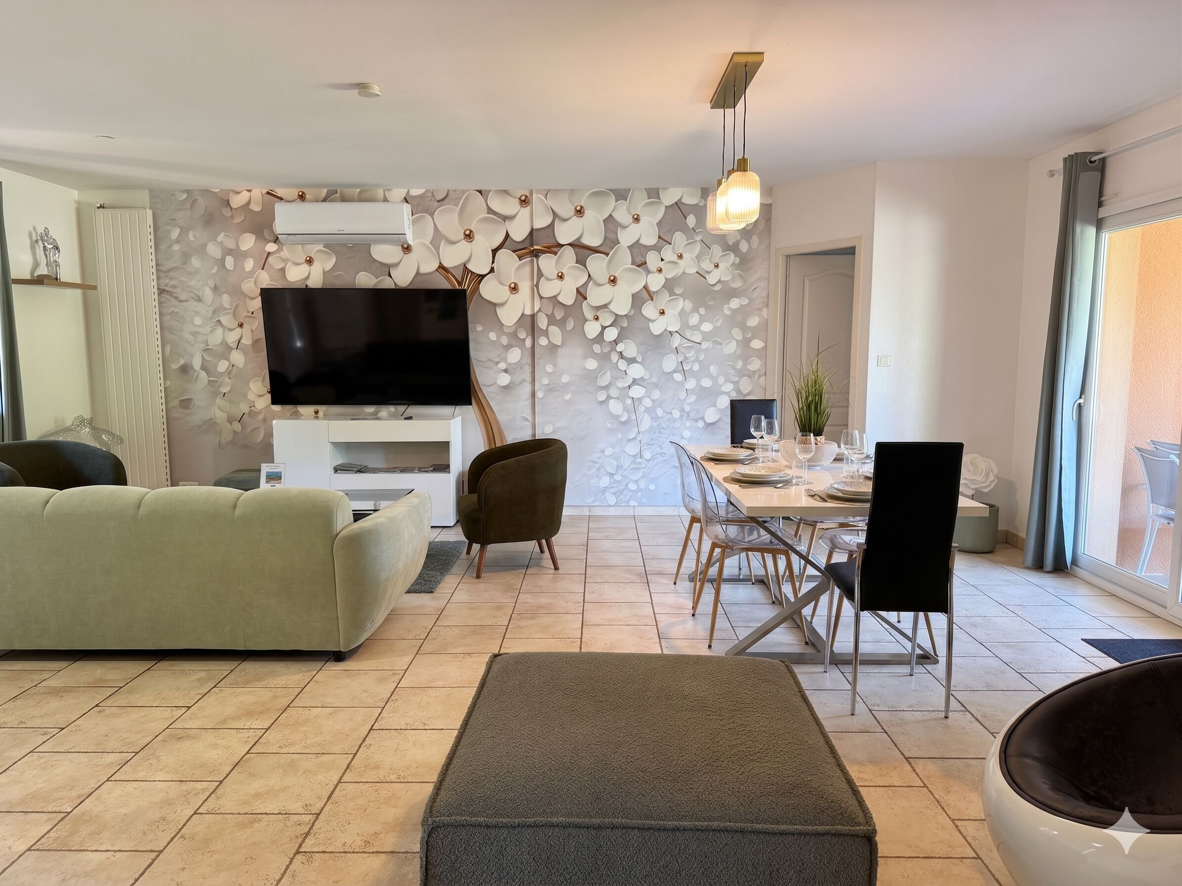 Een moderne woonkamer met een flatscreen televisie, een bank, een eettafel voor vier personen en een groot raam met uitzicht.