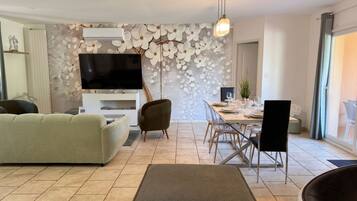 Een moderne woonkamer met een flatscreen televisie, een bank, een eettafel voor vier personen en een groot raam met uitzicht.