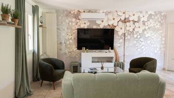 Een woonkamer met een bank, twee fauteuils, een televisie en een decoratieve wand.