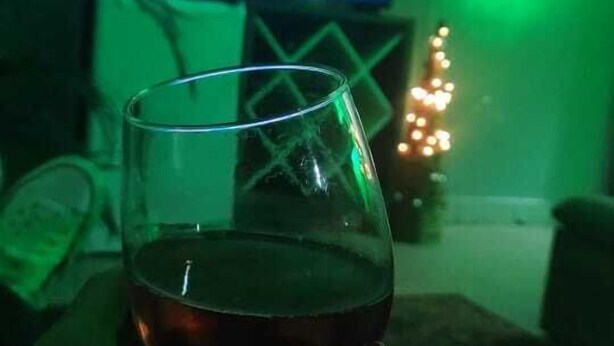 A glass of red wine on a table with a television displaying a landscape in the background.