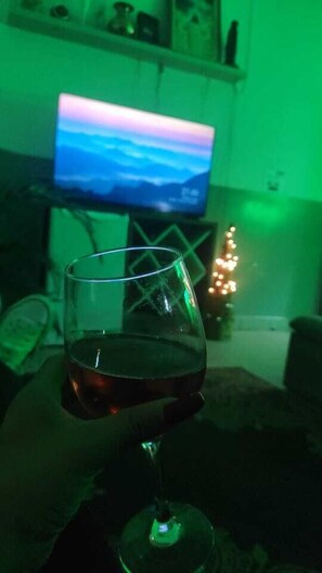 A glass of red wine on a table with a television displaying a landscape in the background. - Hostel Lize (Guarulhos)