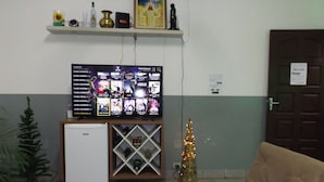A living room with a television, a small refrigerator, a Christmas tree, and a couch.