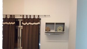 A bedroom with a bed, curtains, a window with a shelf, and a vase with flowers.