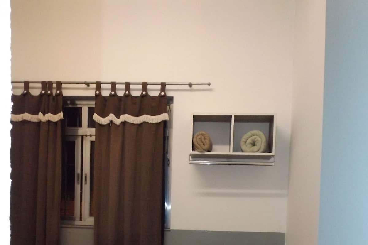 A bedroom with a bed, curtains, a window with a shelf, and a vase with flowers.