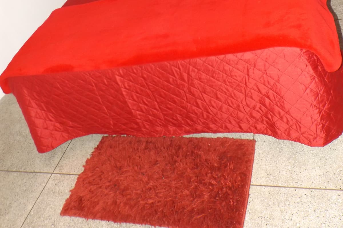 A bed with red bedding and a matching red rug, a wooden headboard, and a small shelf with a decorative item.