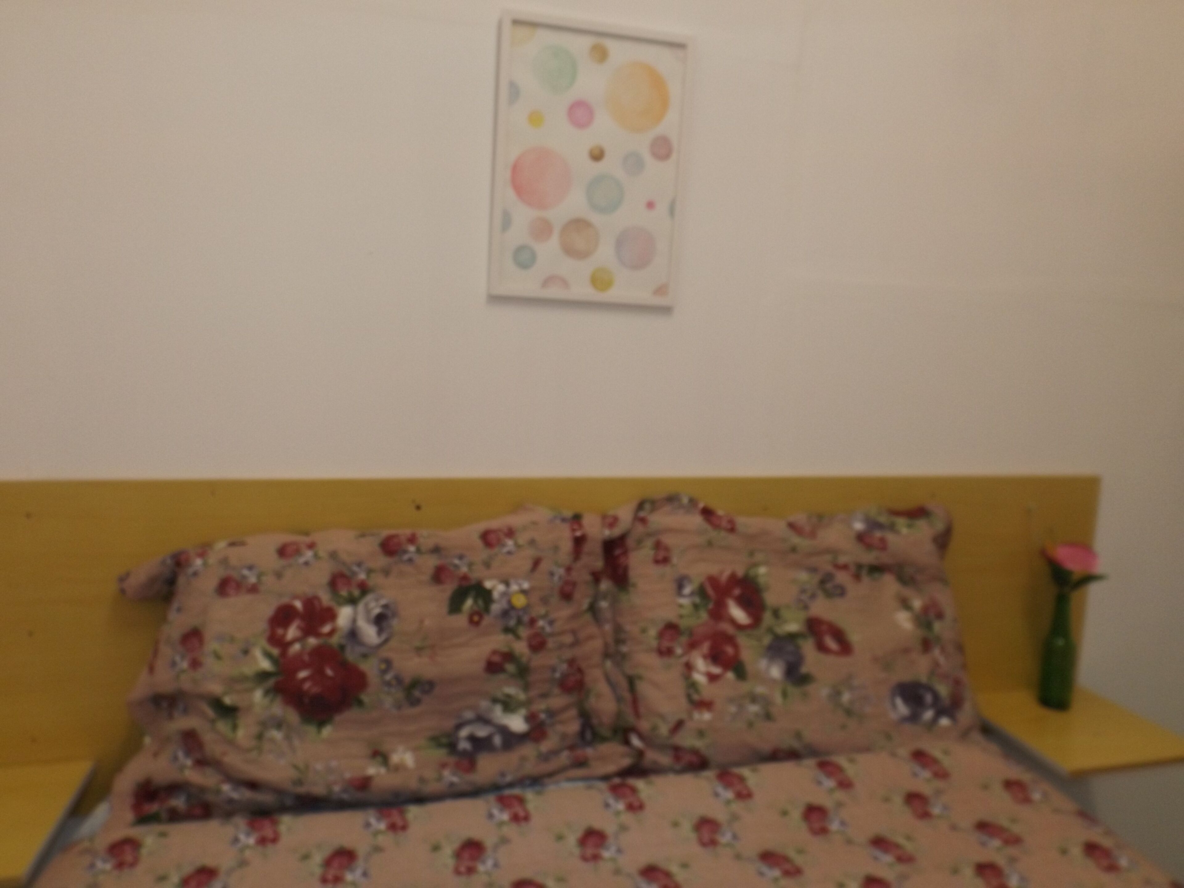 A bed with floral bedding, a wall with a circular pattern, and a nightstand with a vase.