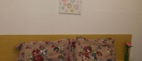 A bed with floral bedding, a wall with a circular pattern, and a nightstand with a vase.