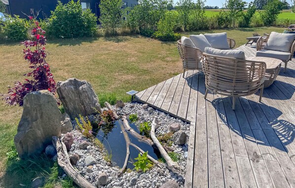Una terraza de madera con mobiliario de mimbre, un pequeño estanque y abundante vegetación.