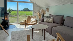 Un salon chaleureux avec une cheminée, un canapé, un fauteuil et une vue sur un champ verdoyant.