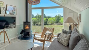 Un salon chaleureux avec un poêle à bois, un canapé, un fauteuil et un téléviseur.