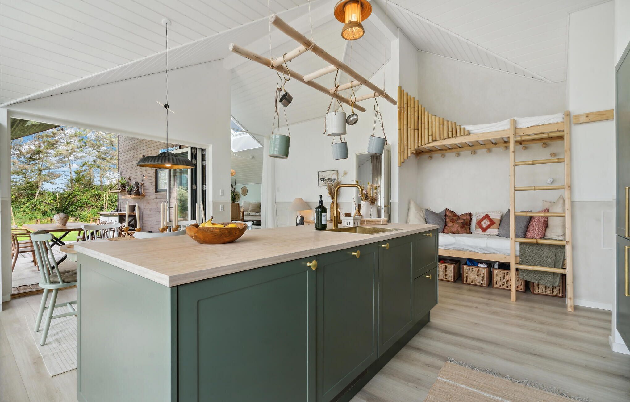A modern kitchen with a central island, a dining area with outdoor seating, and a loft bedroom with a wooden ladder.